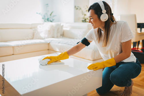 The young woman is cleaning the living room wearing yellow gloves