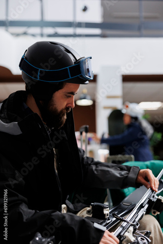 Close-up of caucasian traveler adjusting ski gear in hotel lobby. Male tourist, wearing winter jacket and ski goggles, ensuring safety of wintersports equipment. Ready to explore ski resort for skiing