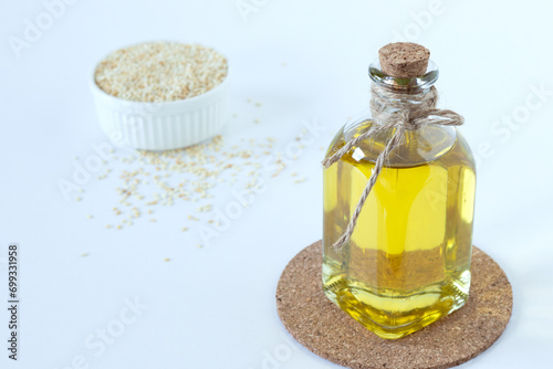 Natural sesame oil in glass bottle with a bowl of toasted seeds on white background.