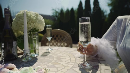 Close-up. The bride holds a glass of sparkling champagne in her hand. On a sunny wedding day, white wine is on the table outdoors. The bubbles in the glass rise up. Holiday wedding concept. photo