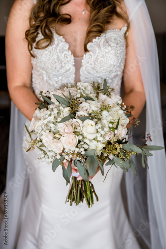 Vertical color photo of bride holding bouquet of white and soft pink flowers on her wedding day