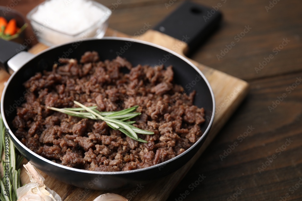 Fried ground meat in frying pan and rosemary on wooden table, closeup. Space for text Fried ground meat in frying pan and rosemary on wooden table, closeup. Space for text