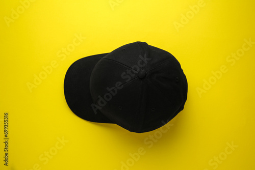 Stylish black baseball cap on yellow background, top view
