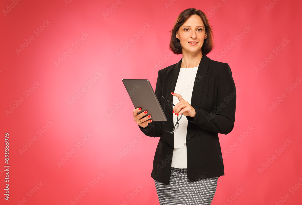 confident business woman with a tablet on a pink background looks into the frame confident business woman with a tablet on a pink background looks into the frame