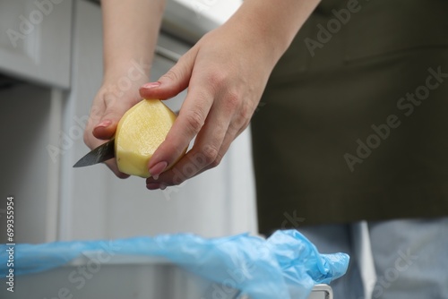 Woman peeling fresh potato with knife above garbage bin indoors, closeup