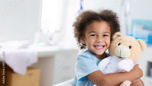 Cheerful African American girl cuddling with her teddy bear in a bright hospital room, embodying joy and comfort.