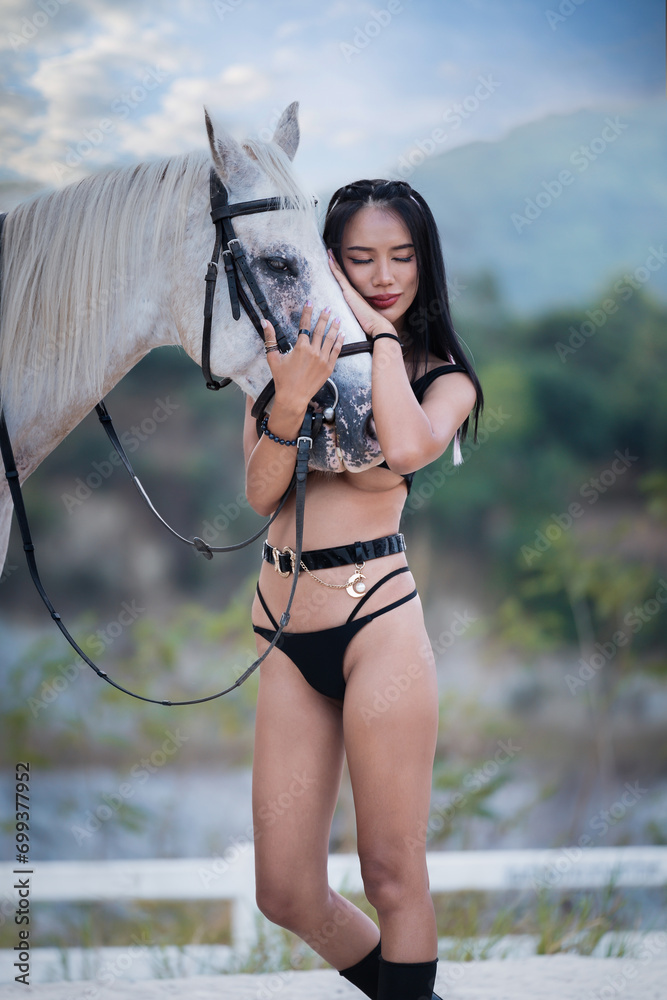 Obraz premium Beautiful young lady wearing in black sexy lingerie riding a horse in forest. Portrait Of Woman With Horse, Model and horse. Young woman with a white horse in the summer on the field close-up.
