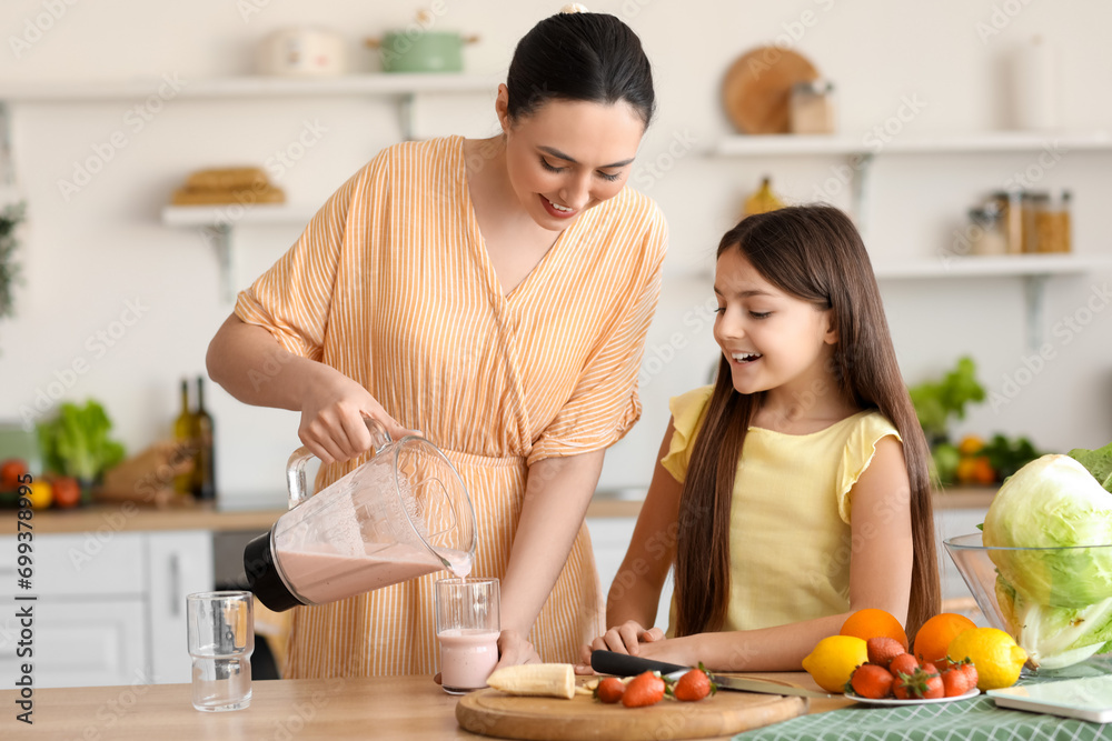 Young woman with her little daughter pouring fresh smoothie into glass in kitchen Young woman with her little daughter pouring fresh smoothie into glass in kitchen