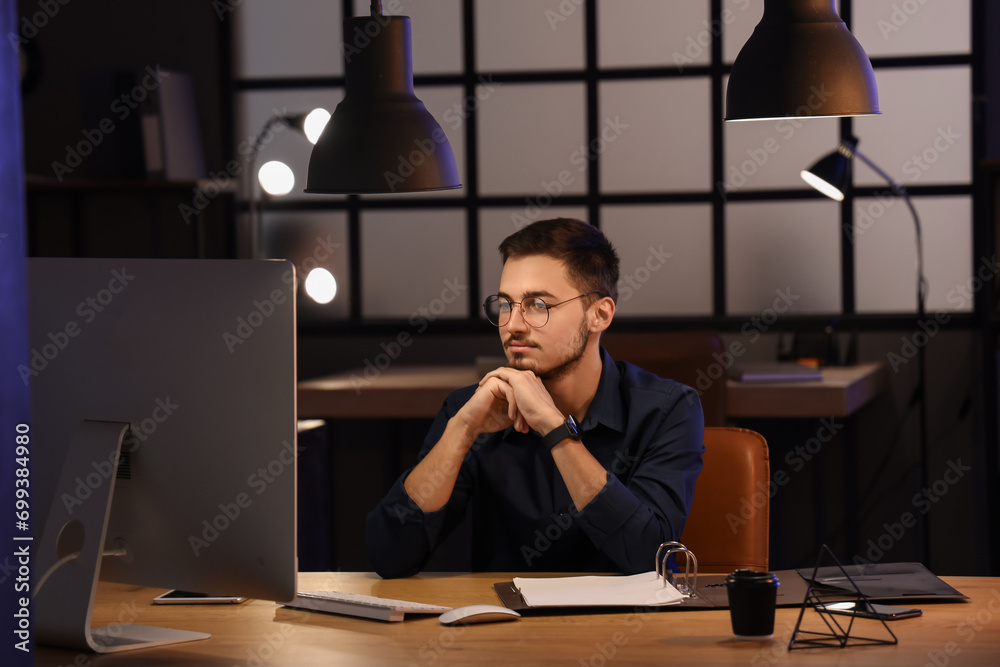 Handsome young man working with computer in office at night