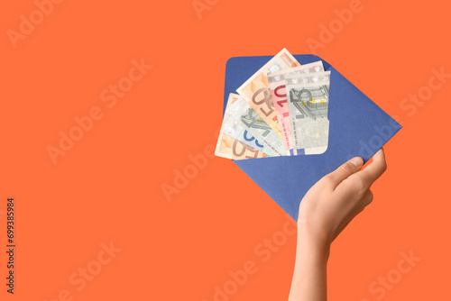 Female hand with envelope and money on orange background
