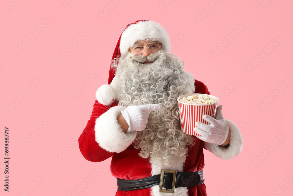 Santa Claus pointing at tasty popcorn on pink background