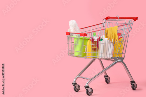 Shopping cart with cleaning supplies on pink background