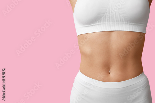 Young woman with flat belly on pink background, closeup. Plastic surgery concept