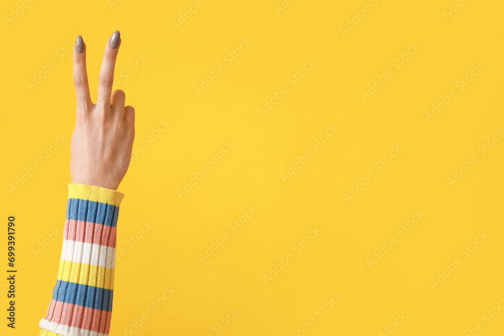 Fototapeta premium Young woman showing peace sign on yellow background