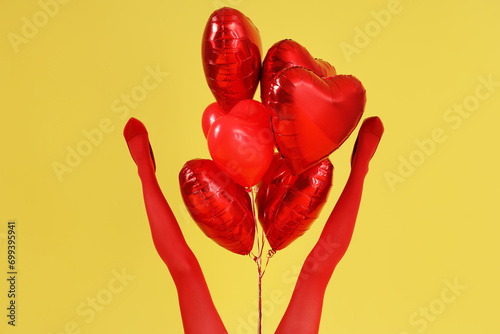 Legs of young woman with heart shaped air balloons on yellow background. Valentine's Day celebration photo