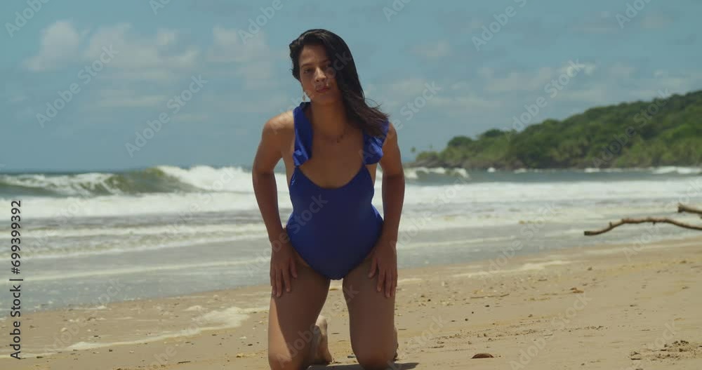 Reveling in the Caribbean magic of Trinidad's beach, a Hispanic girl donned in a bikini celebrates the sun and sand kneel in the sand