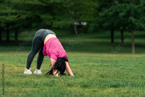 beautiful brunette woman doing stretching, yoga and exercises, in a green grass park wearing sportswear