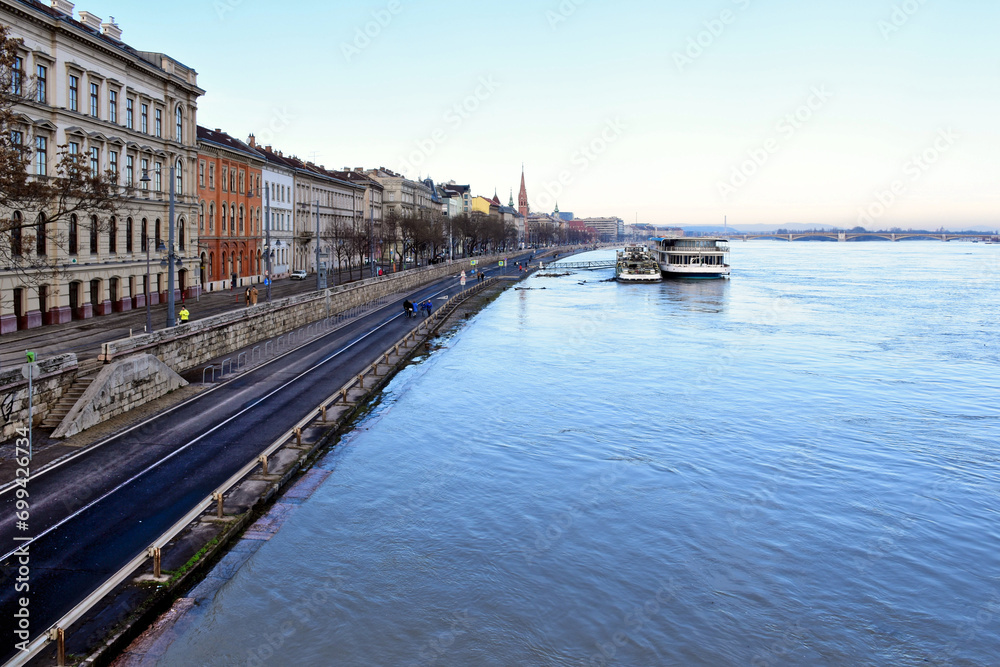 Budapest, Hungary - 12. 26. 2023. Aerial view of the flooding Danube river from the Chain bridge. high water level reaching the quay and asphalt low road closed to car traffic. pedestrians strolling