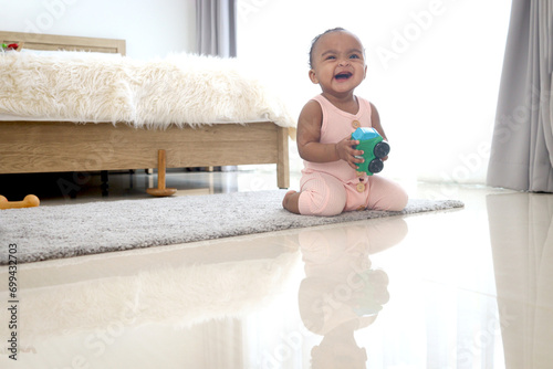 Happy smiling African cute toddle baby infant kid holding toy while crawling on floor in bedroom at home. Happy child with reflection on the floor, happy childhood photo