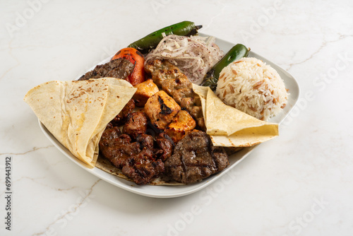 Mixed grill made of meat, chicken and fried quiche, served on a white plate with delicious baldo rice and fried potatoes.