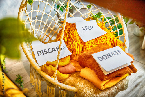 Signs with the words keep, donate, discard and fashion clothes folded in stacks in cozy room. The concept of cluttering, decluttering. Background photo