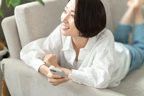 ソファーで横になってスマホを操作する女性 photo