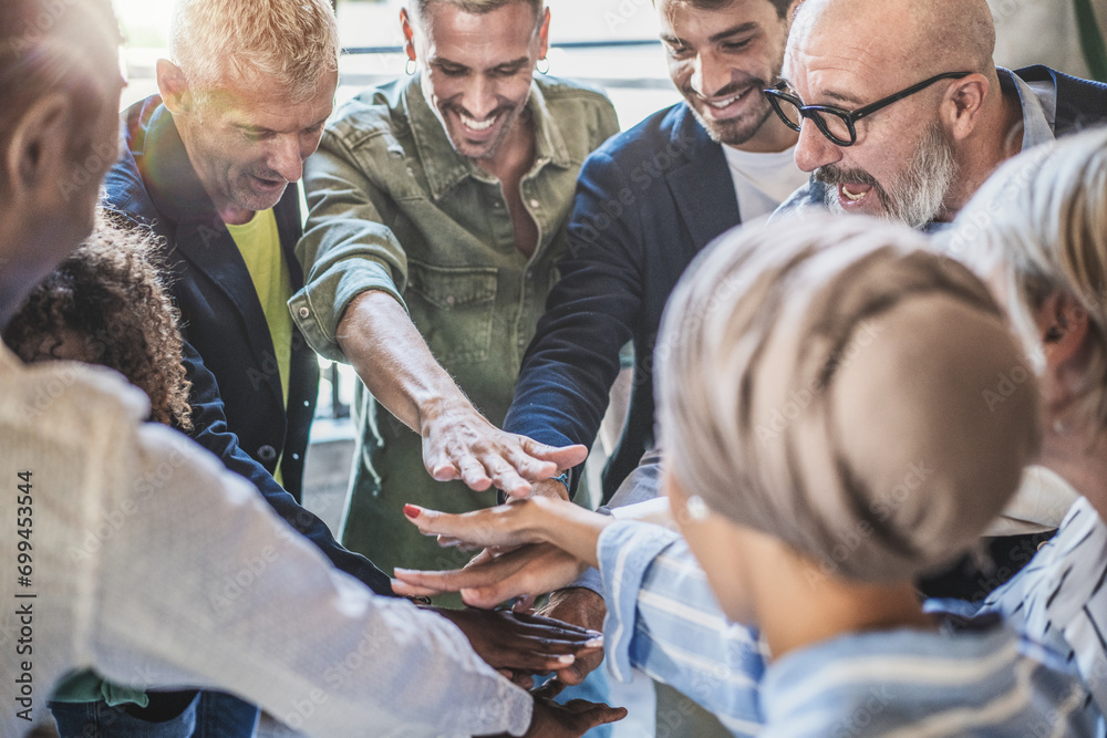 © Lomb - Diverse business team stacks hands in unity, showcasing teamwork and partnership in a dynamic workplace.