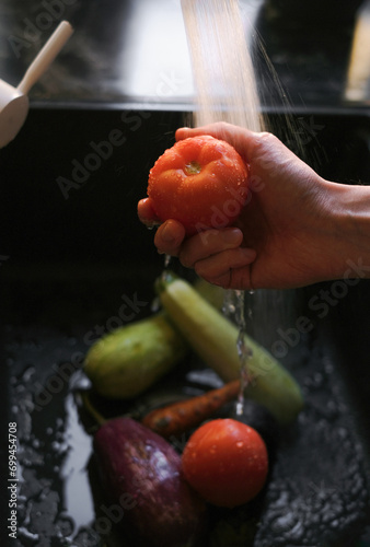 a man washes organic tomatoes and other vegetables under running water in the sink