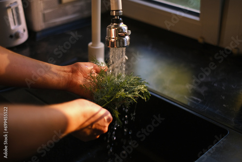 Woman rinses dill and parsley under running water close-up of hands photo