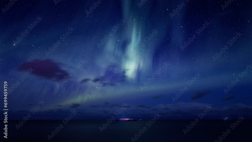 Lofoten winter landscape. A wide angle view of an islet in the sea under the northern lights in a polar winter blue sky filled with clouds and stars. Lofoten Islands, Northern Norway.