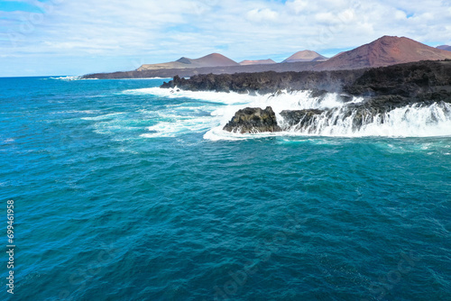 Panoramic aerial view of Los Hervideros. Southwest coast, rugged volcanic coast, strong surf, sea caves, red lava hills. Lanzarote, Canary Islands, Spain