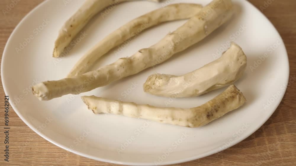 Peeled horseradish roots on a white plate. Slow motion. Peeled horseradish roots on a white plate. Slow motion.