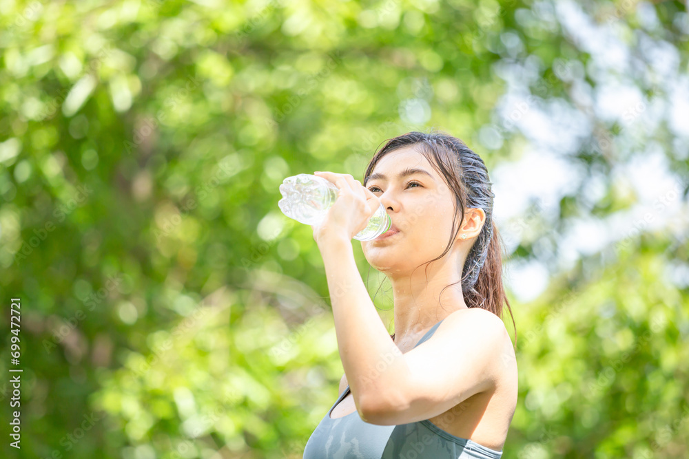 Sportswoman drinking water after working out exercising, Athlete young woman with a plastic water bottle at green park Sportswoman drinking water after working out exercising, Athlete young woman with a plastic water bottle at green park