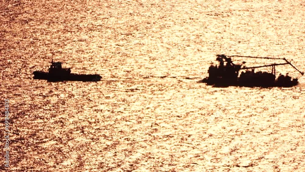 Tug boat pulls a barge loaded with harbor cranes across calm seas at ...
