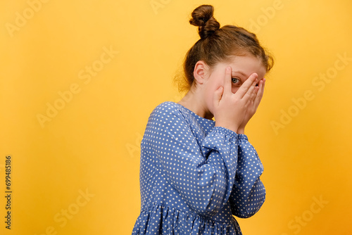 Portrait of shocked little girl kid covers face with hands, posing isolated over yellow background, child watching horror film, movie, reaction, facial expression. Children and human emotions concept photo