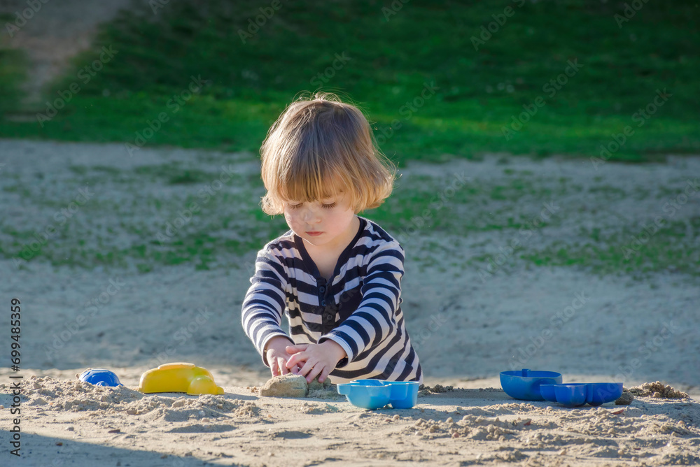 Cute little child boy having fun playing with sand and colorful toys in the park, beautiful summer sunny day in children playground. Selective focus