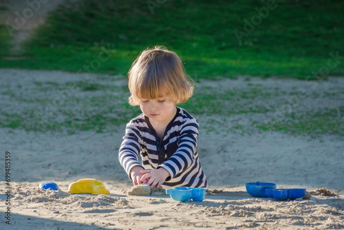 Obraz na płótnie Cute little child boy having fun playing with sand and colorful toys in the park, beautiful summer sunny day in children playground. Selective focus w salonie
