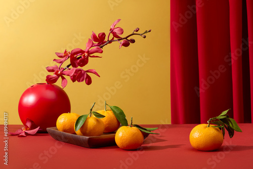 Tangerines displayed on wooden dish and a flower pot decorated on red surface. During Chinese New Year  red is said to symbolize luck and happiness