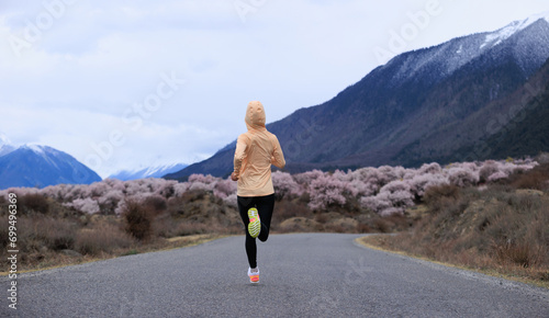 Woman running in spring tibet,peach flowers blooming and snow capped mountains in the background, China