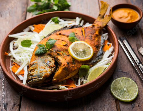 Tandoori Pomfret fish cooked in a clay oven and garnished with lemon , mint, cabbage and carrot salad photo