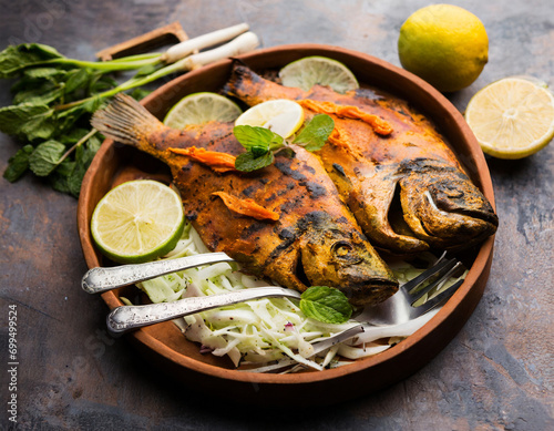 Tandoori Pomfret fish cooked in a clay oven and garnished with lemon , mint, cabbage and carrot salad photo