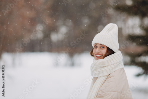 Happy smiling young woman portrait dressed coat scarf hat and mittens enjoys winter weather at snowy winter park.