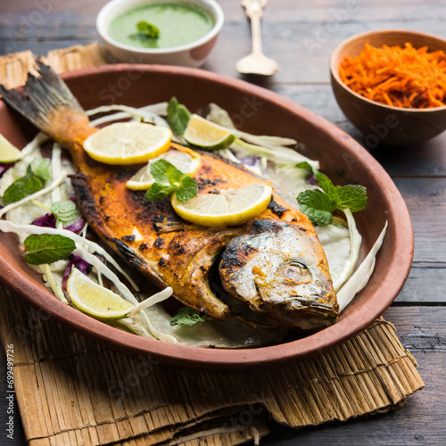 Tandoori Pomfret fish cooked in a clay oven and garnished with lemon , mint, cabbage and carrot salad