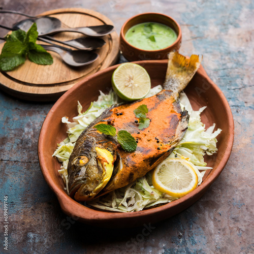 Tandoori Pomfret fish cooked in a clay oven and garnished with lemon , mint, cabbage and carrot salad photo