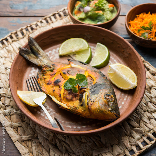 Tandoori Pomfret fish cooked in a clay oven and garnished with lemon , mint, cabbage and carrot salad photo