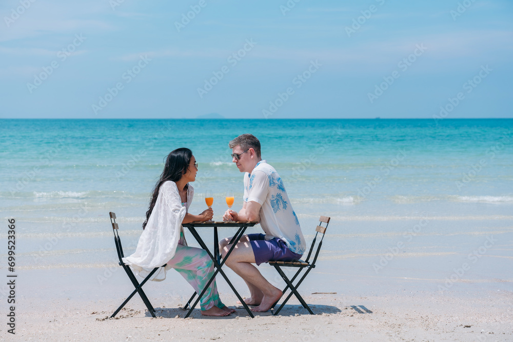 Happy and loving young couple drink orange juice at tropical beach. Couple Enjoying Fun and Romance by the Ocean.