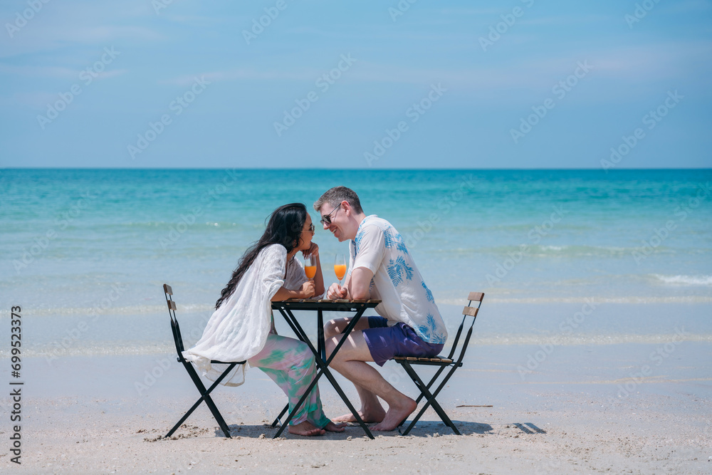 Happy and loving young couple drink orange juice at tropical beach. Couple Enjoying Fun and Romance by the Ocean.