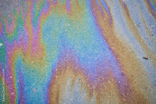 Multi-colored poisonous spots of spilled gasoline on wet pavement during rain.