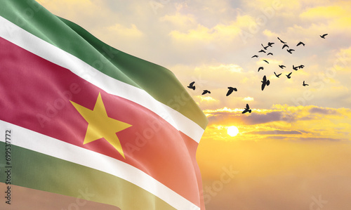Waving flag of Suriname against the background of a sunset or sunrise. Suriname flag for Independence Day. The symbol of the state on wavy fabric.