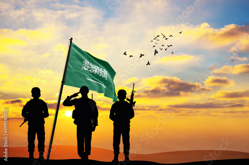 Silhouettes of soldiers with the Saudi Arabia flag stand against the background of a sunset or sunrise. Concept of national holidays. Commemoration Day. photo